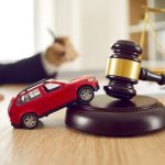 Little red toy automobile on table with sound block and gavel. Small car model on wooden desk with judge's hammer. Car accident, drunk driving, lawsuit, court of law, justice, lawyer services concept